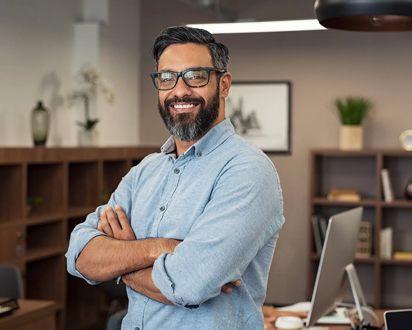 Smiling man in glasses with arms crossed in an office