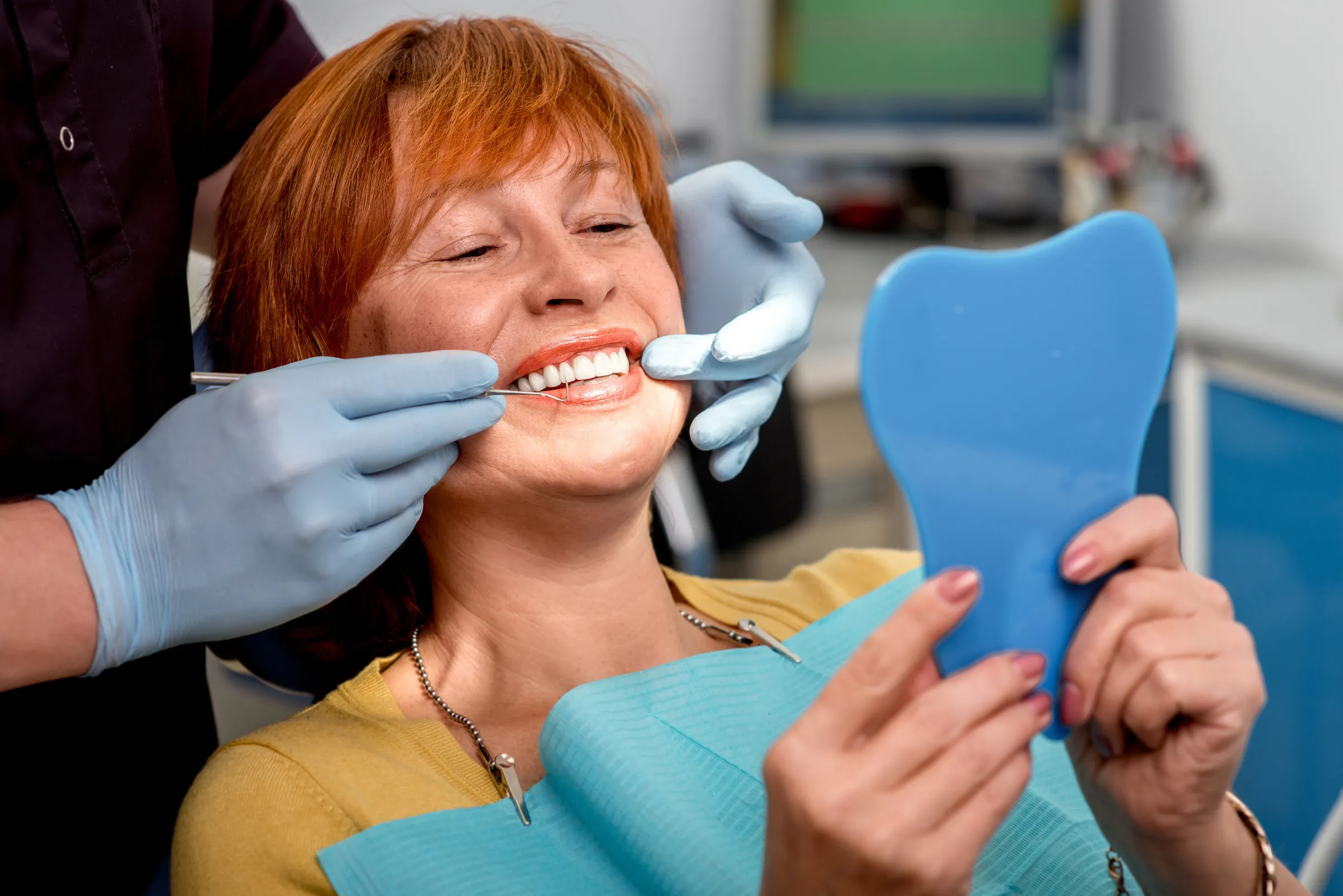 Smiling woman checking her teeth in a hand mirror at the dentist