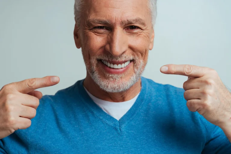 Smiling older man pointing to his teeth with both hands