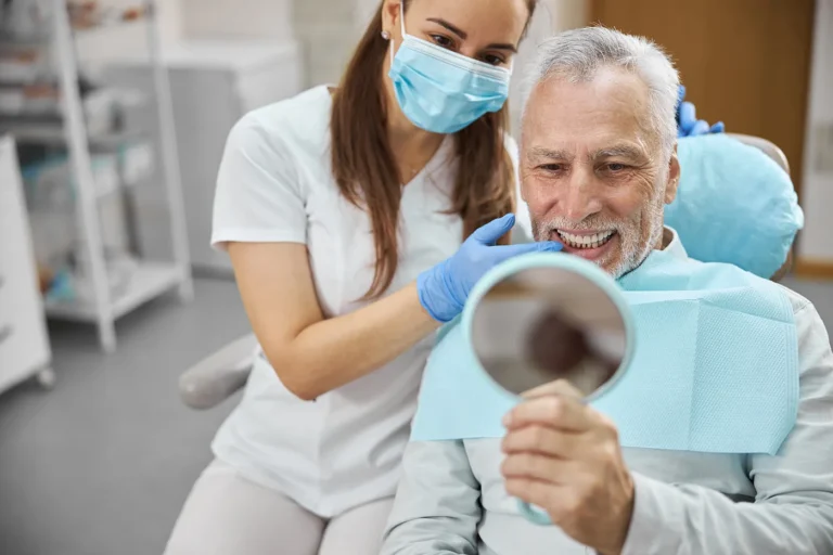 Older man checking his smile in a hand mirror with his dentist