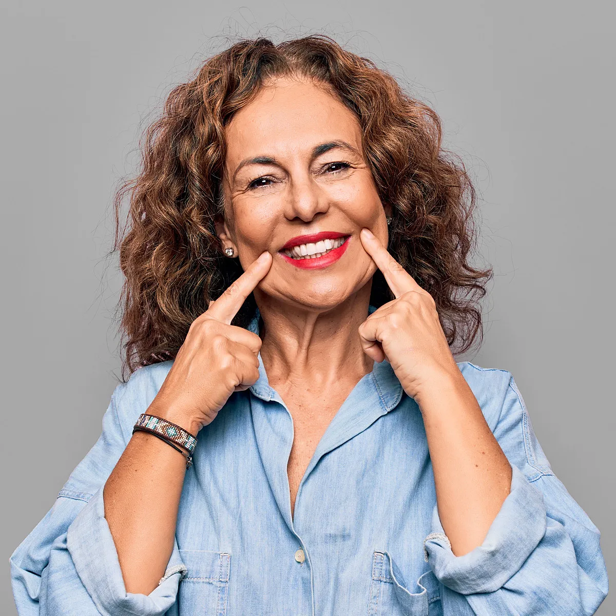 Smiling woman with curly hair pointing to her smile